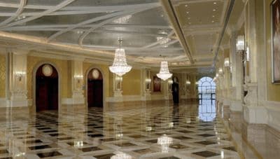 Sweeping ballroom with two crystal chandeliers, natural light, gold wall treatments and ceiling details