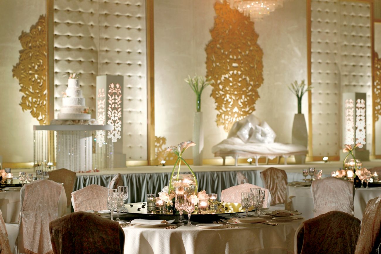 White-and-gold event space with round tables and a dais bedecked in flowers and candles