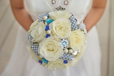 Bride holds a tightly gathered bouquet of white roses and sparkly accents in clear and blue crystal