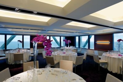 A banquet room with formally set tables and large windows overlooking the sea