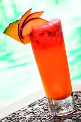 Tall highball glass with bright orange drink and pineapple wedge garnish