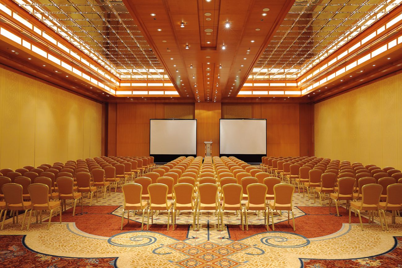 Large, gold-themed ballroom set up for a theater-style conference and featuring two screens