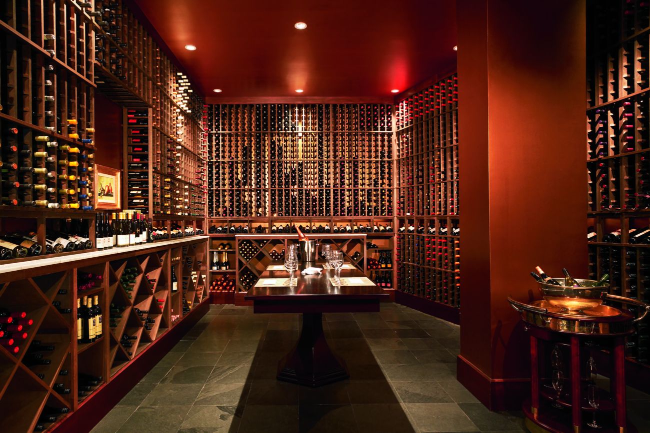 Room with a long table in the middle and wall shelves filled with wine bottles