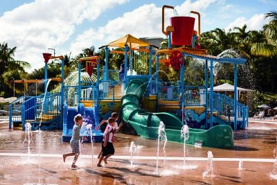 Children run around an outdoor playground with slides and water shooting from the ground