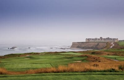 A golf course next to the ocean with a cliff-top building in the distance