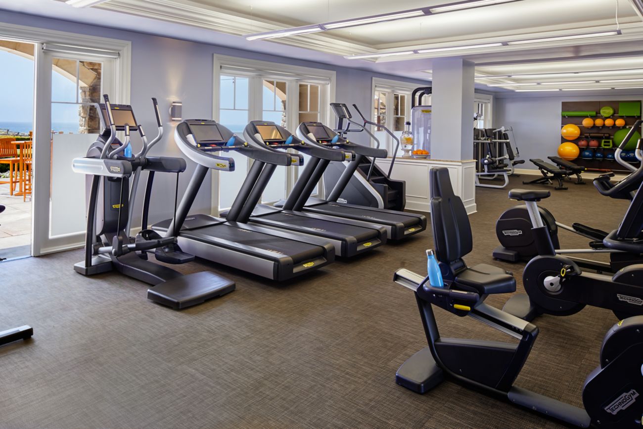 Row of treadmills and an elliptical next to an open door leading to a furnished patio