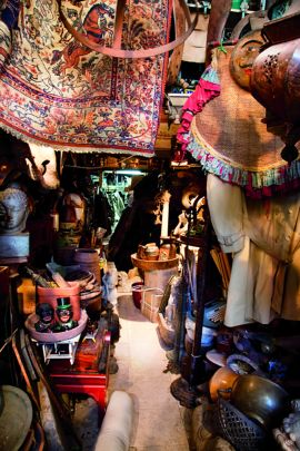 Narrow space packed full to bursting with rugs, bric-a-brac and dishes