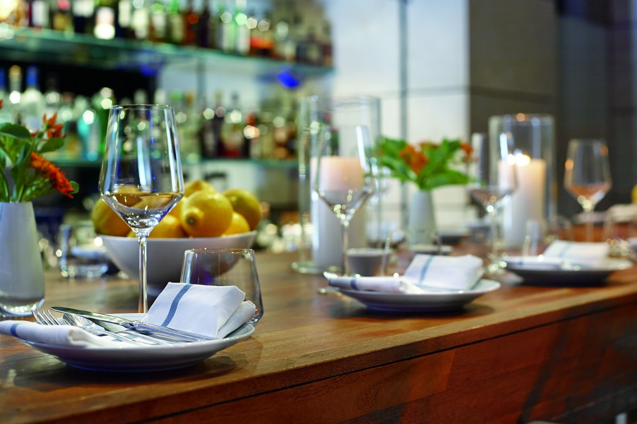Place settings on a wooden bar with shelves of liquor in the background
