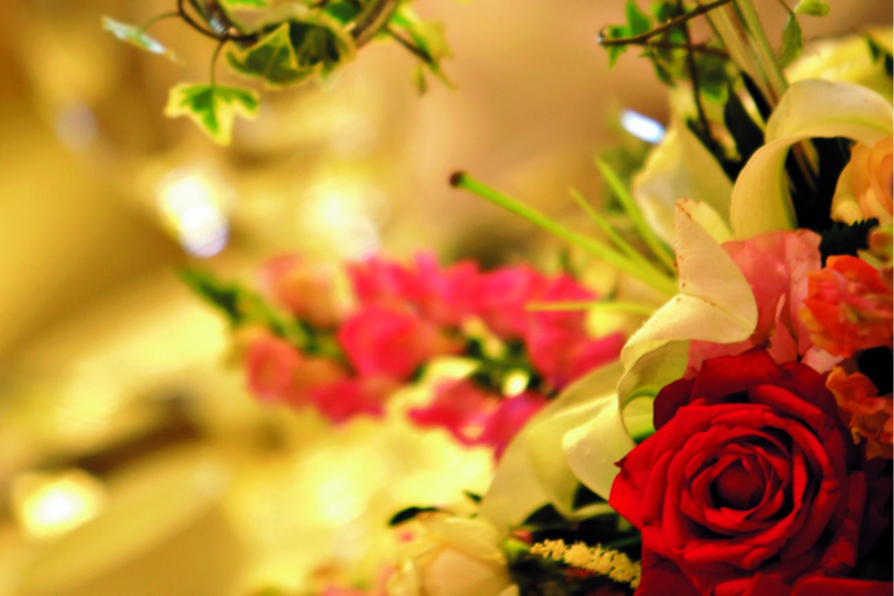 Close-up of a floral arrangement?s red roses and white lilies with a blurred table setting in the background