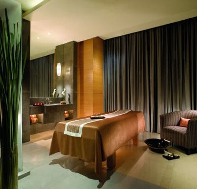 Room with a massage table, an armchair with a bowl in front of it, and a tub with candles on the ledge