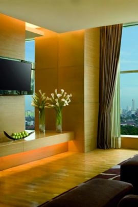 Room with a large window overlooking a city with a row of armchairs and foot stools facing a wall-mounted flat-screen TV