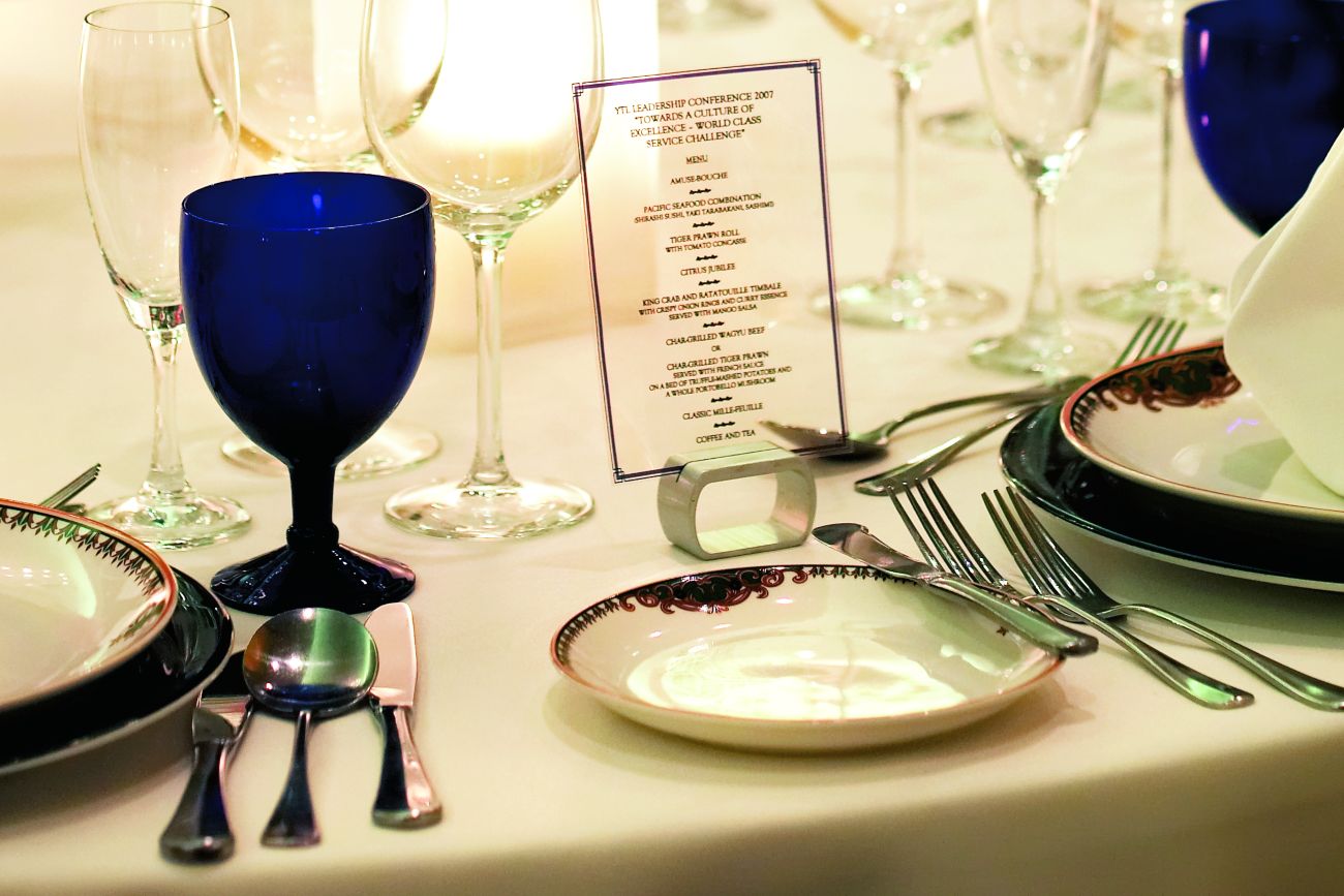 Place setting with a menu printed on transparent material, plus blue goblets, clear wineglasses and china