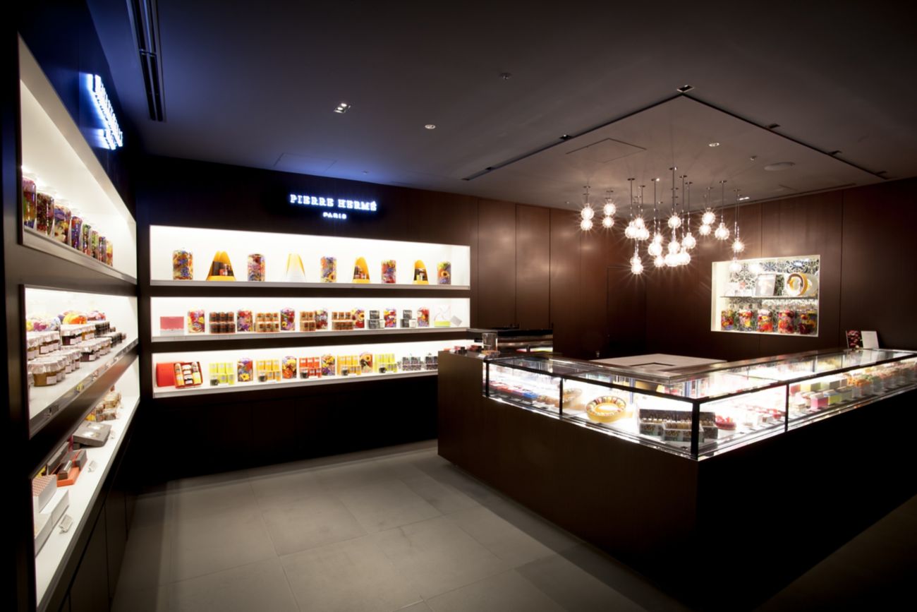 Sleek patisserie with dark wood paneling, illuminated inset shelves, a glass display case and modern light fixtures