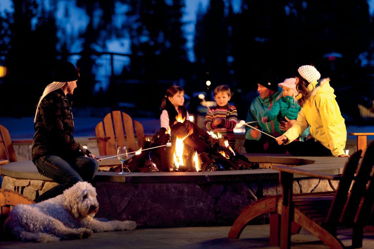 A group of adults and kids around a firepit at night