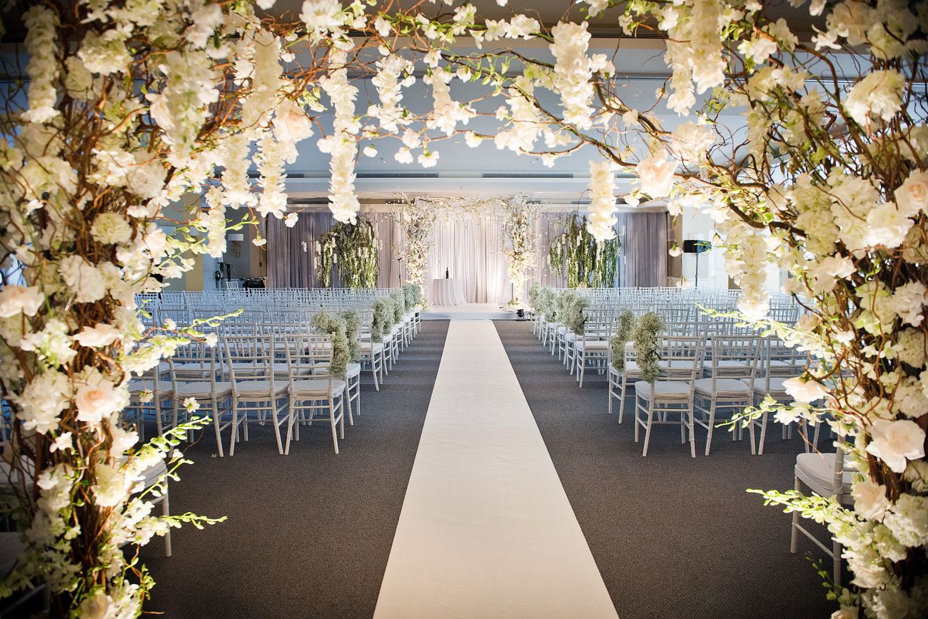 View through a flower-adorned archway at rows of chairs facing the front of an event venue