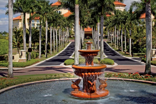 The resort entrance punctuated by a water feature and underscored by a palm tree-lined driveway