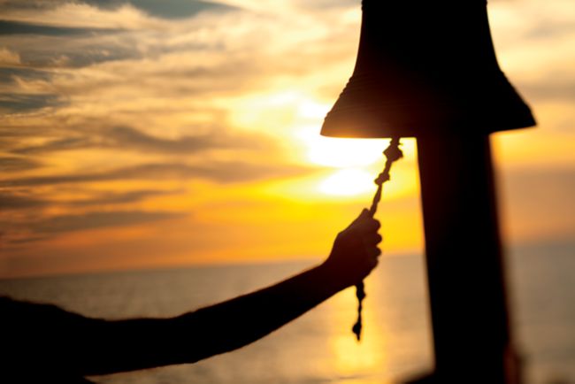 A hand rings a bell at sunrise.