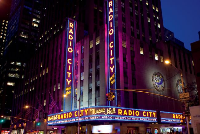The neon lights of Radio City Music Hall glow in magenta and gold during a New York City evening