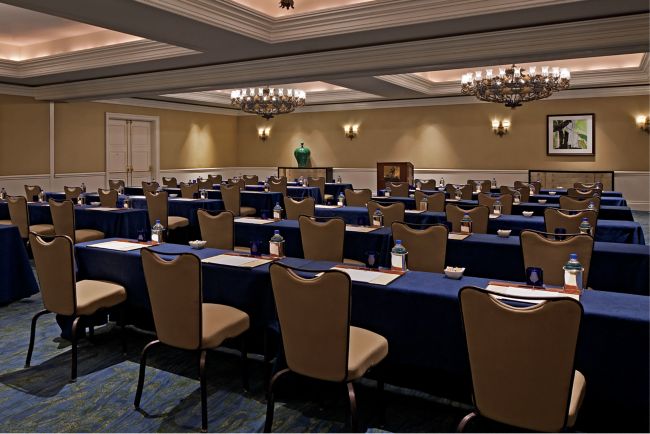 Room with large chandeliers and rows of tables and chairs facing a podium at the front