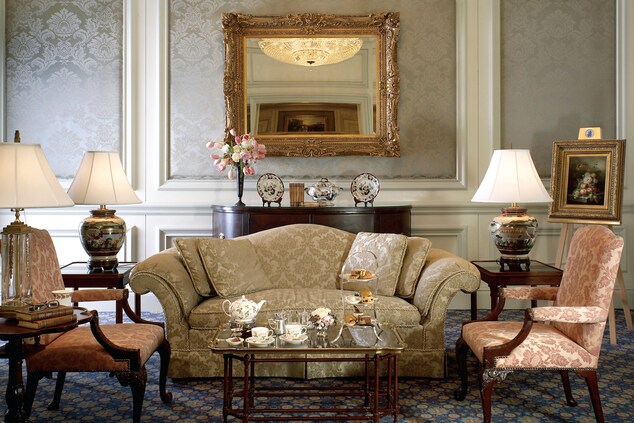 豪華なソファー、アームチェア、金枠の鏡、ティーが用意されたコーヒーテーブルを配置した壁紙の部屋