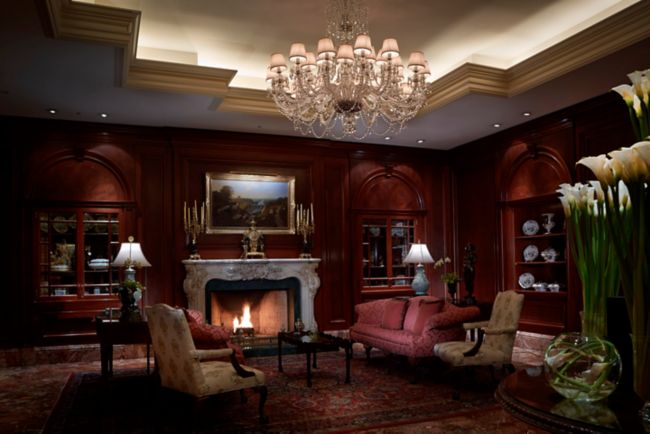 Elegant sitting area with a fireplace, wood-paneled walls, a crystal chandelier and built-in cabinetry with glass fronts