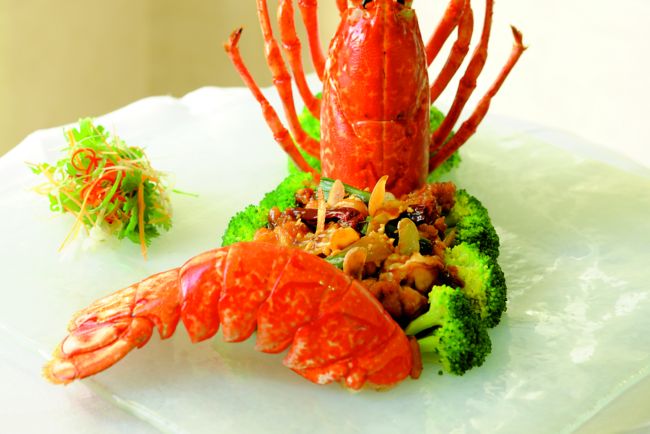Lobster positioned upright on a white plate with broccoli and garnish separating it from the tail