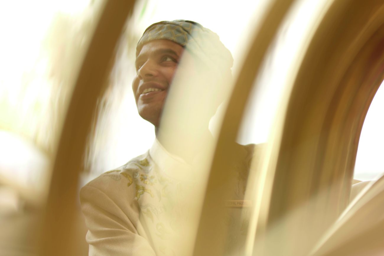 Hotel associate in local attire gazes into the distance as seen through a blurry window