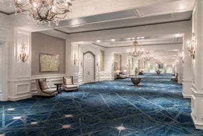 A wide carpeted hallway with chandeliers and seating areas