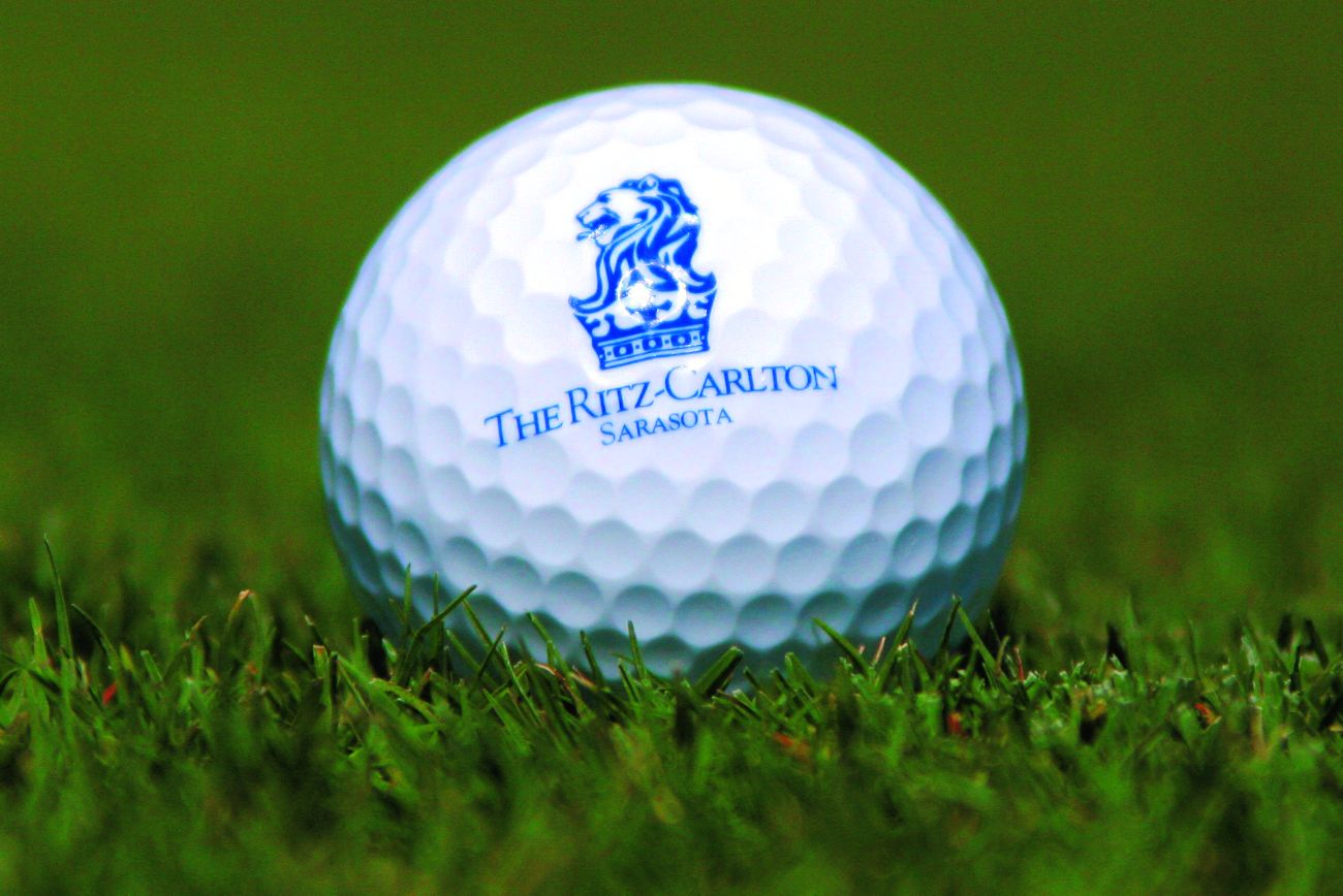 A golf ball with The Ritz-Carlton, Sarasota logo rests on green turf