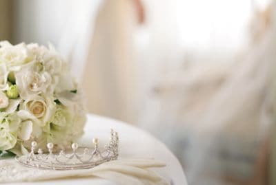 A tightly gathered bouquet of white flowers rests alongside a crystal-and-pearl tiara and white gloves