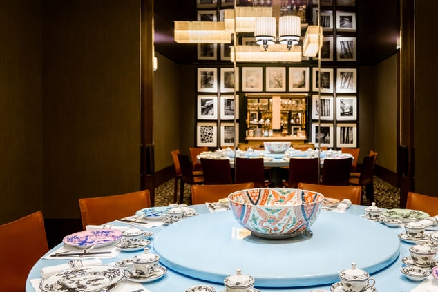 Rust-colored chairs surround a circular, powder-blue table with a lazy Susan and which is set with colorful Chinese plates