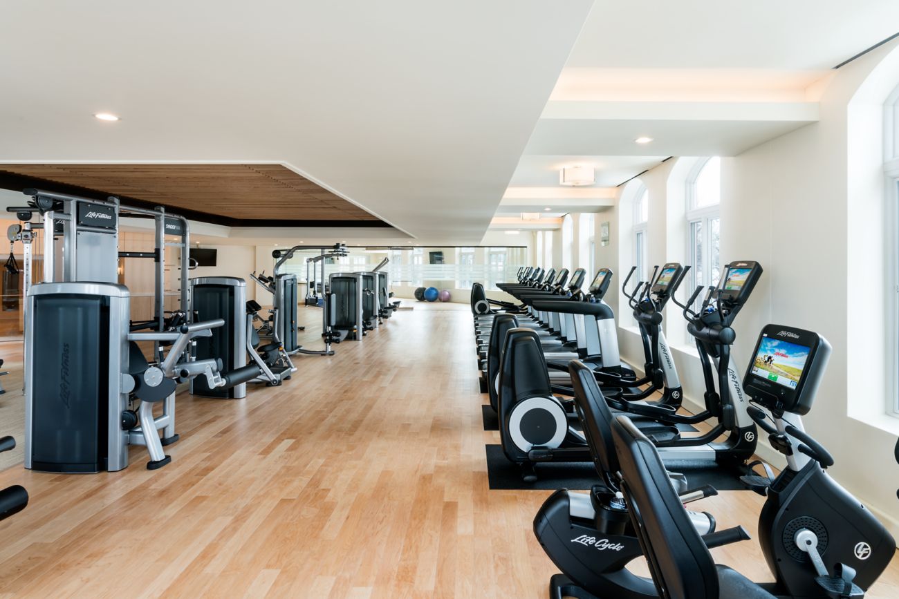 Treadmills, stationary bikes and weight machines facing a wall of windows