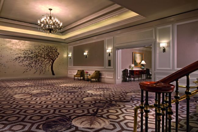 An open space with patterned carpeting, a tree mural, chandelier and small seating area