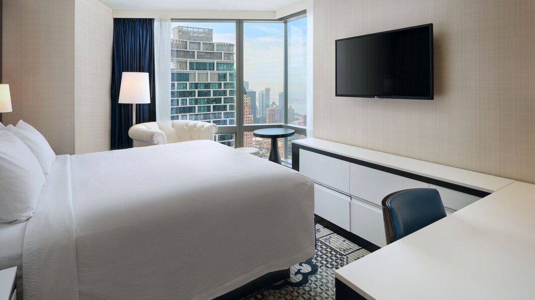 suite de hotel con cama tamaño King, escritorio, televisor y vista a la ciudad de Nueva York