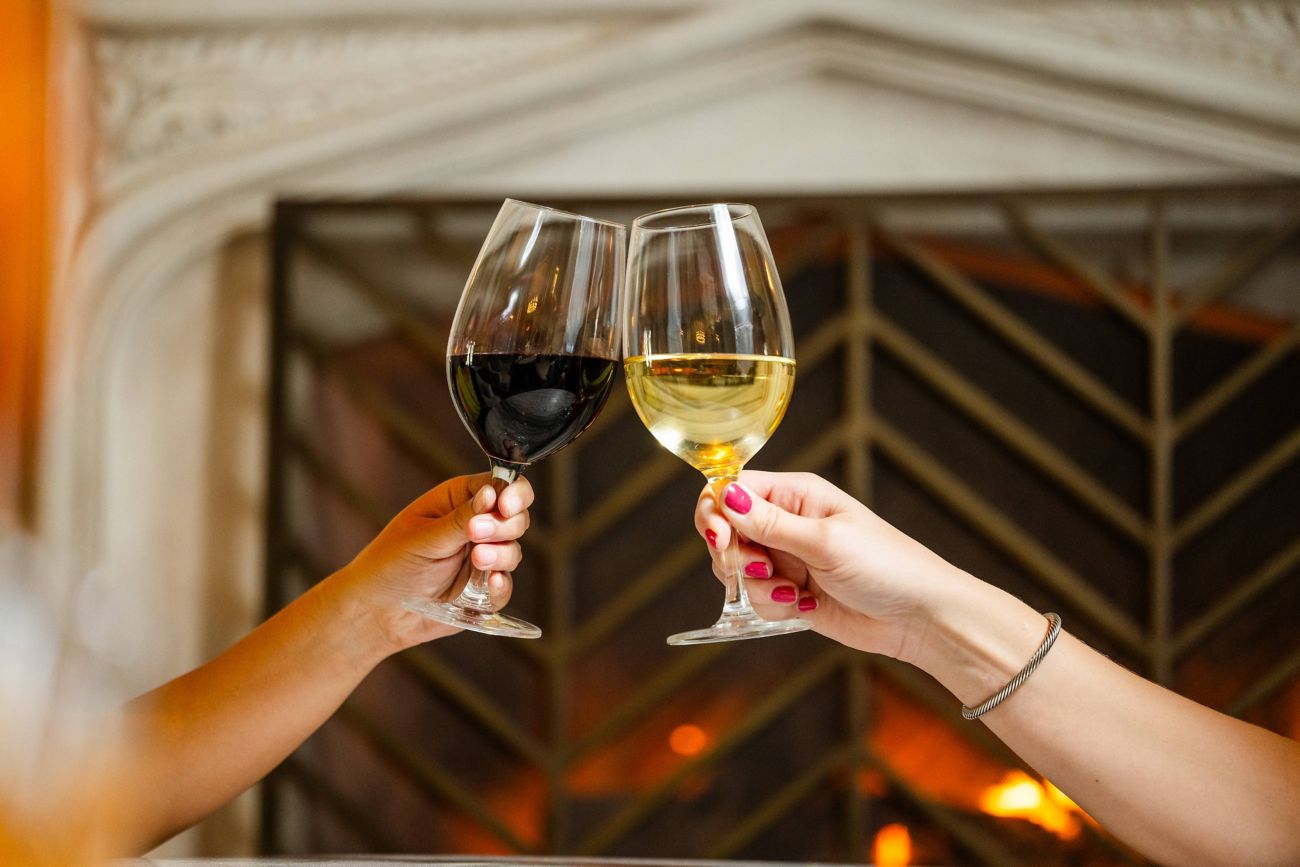 Two people cheers with wine glasses by the firepla
