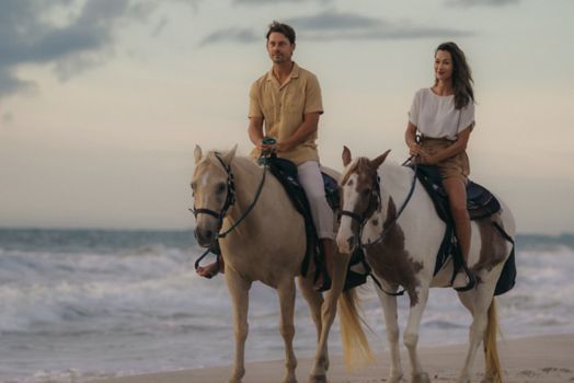 Couple horseback riding on beach.