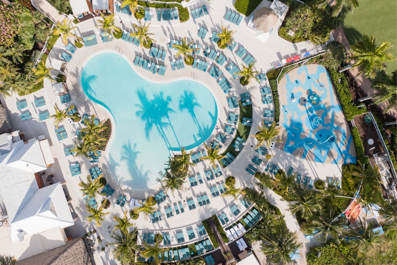 Vista aérea de la piscina y área de recreación infantil con palmeras
