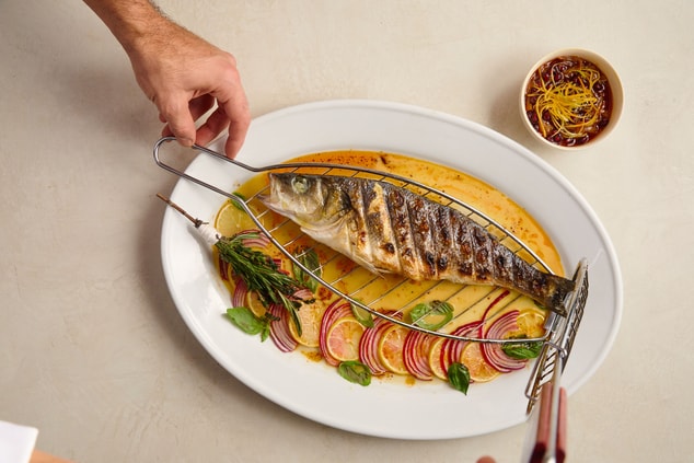 Grilled whole fish on a sauce with garnish.
