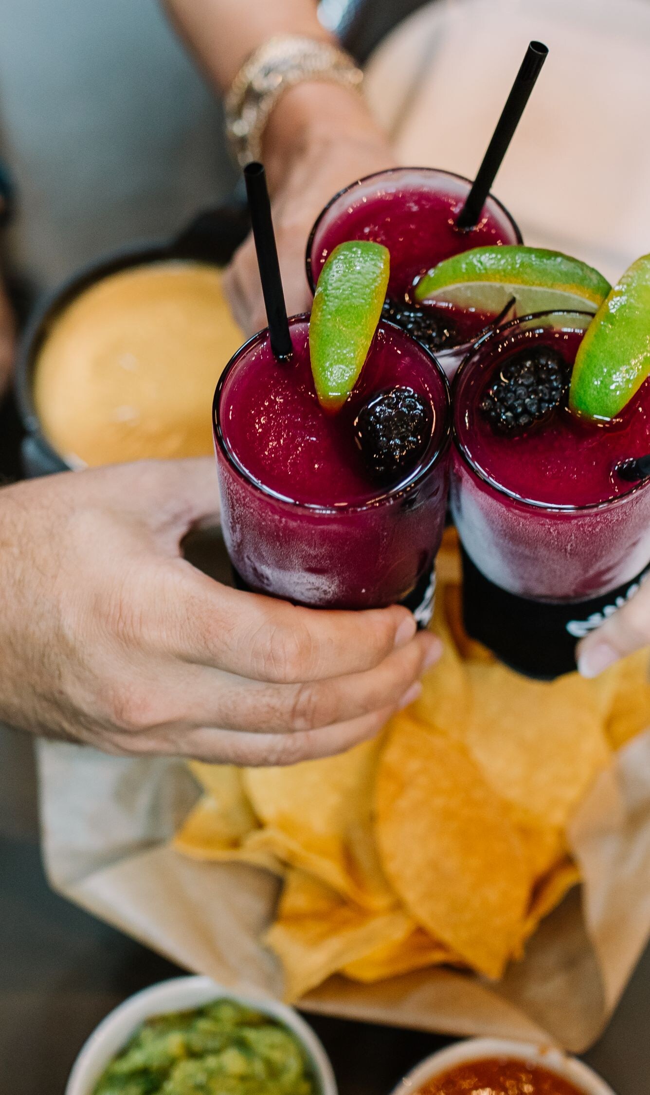 Three people with cocktails cheers over chips