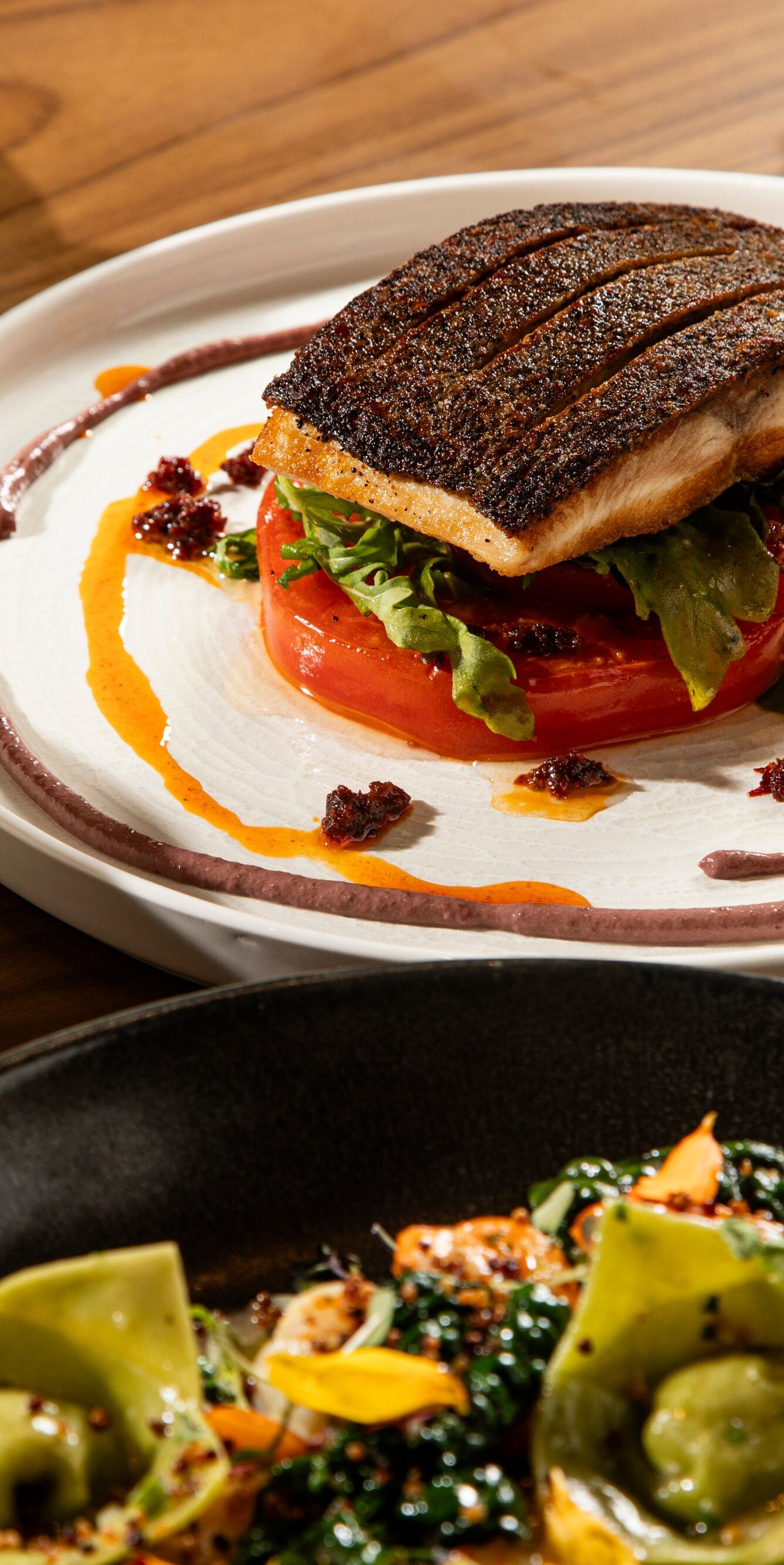 Auf einem Teller angerichteter, gebratener Fisch auf Tomaten und Gemüse
