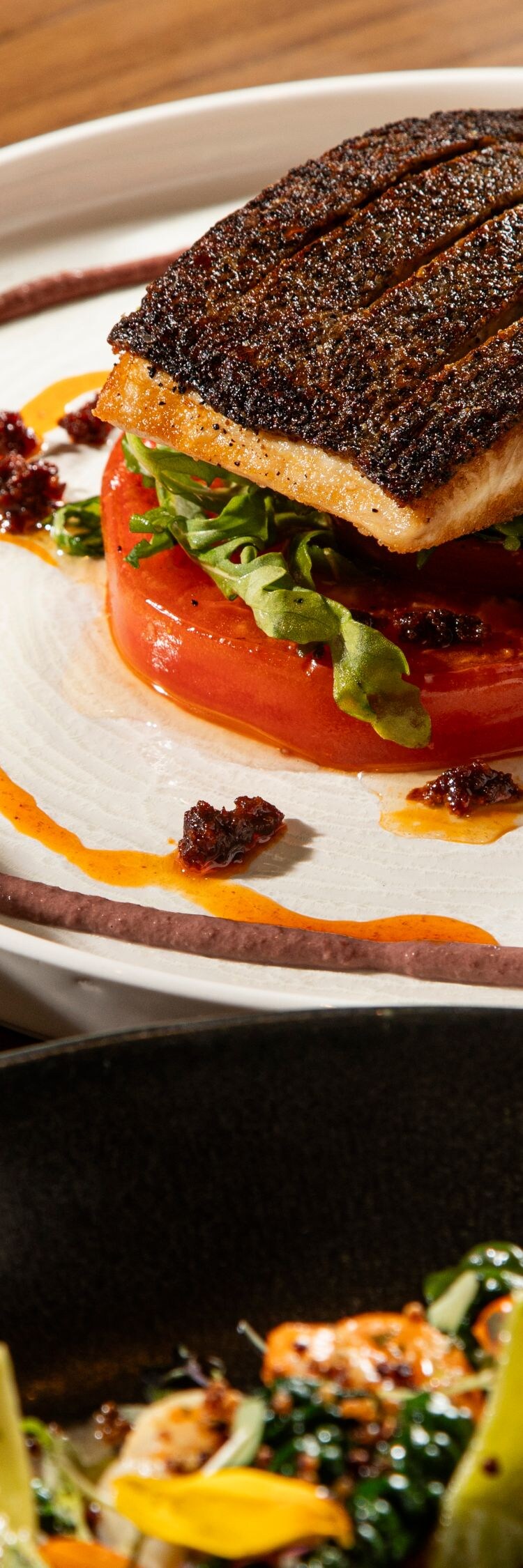 Auf einem Teller angerichteter, gebratener Fisch auf Tomaten und Gemüse