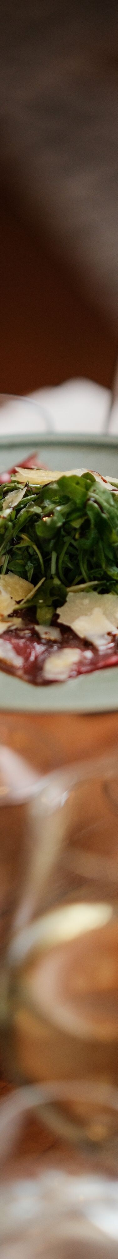 Fork picking up carpaccio from plate being held ab