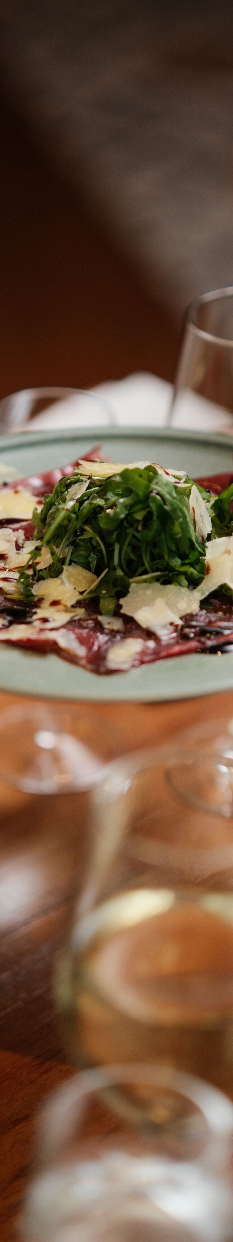 Fork picking up carpaccio from plate being held ab