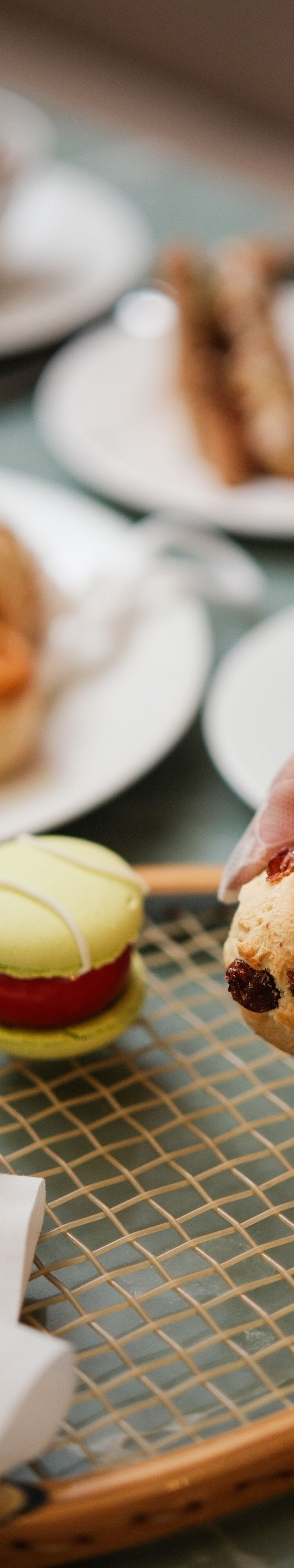 Hand picking up scone beside tea and cakes