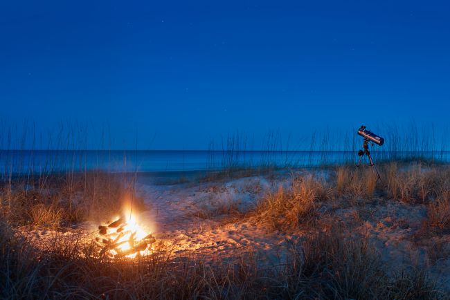 A fire pit on the beach with a telescope in the distance