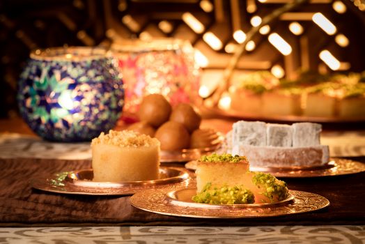 Gold plates bearing sweet treats are presented on an intricately designed table next to colorful, spherical candle holders