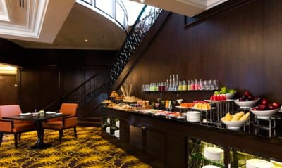 Colorful buffet of fruits, juices and more along a dark wood shelf with seating and a staircase in the background