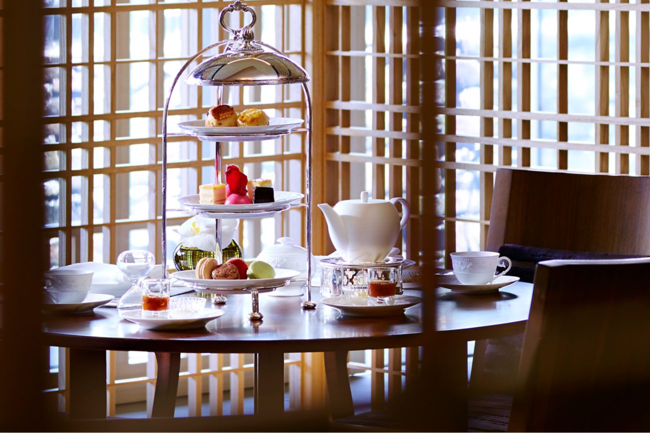 Three chairs around a table with a tiered pastry tower, teapot and cups