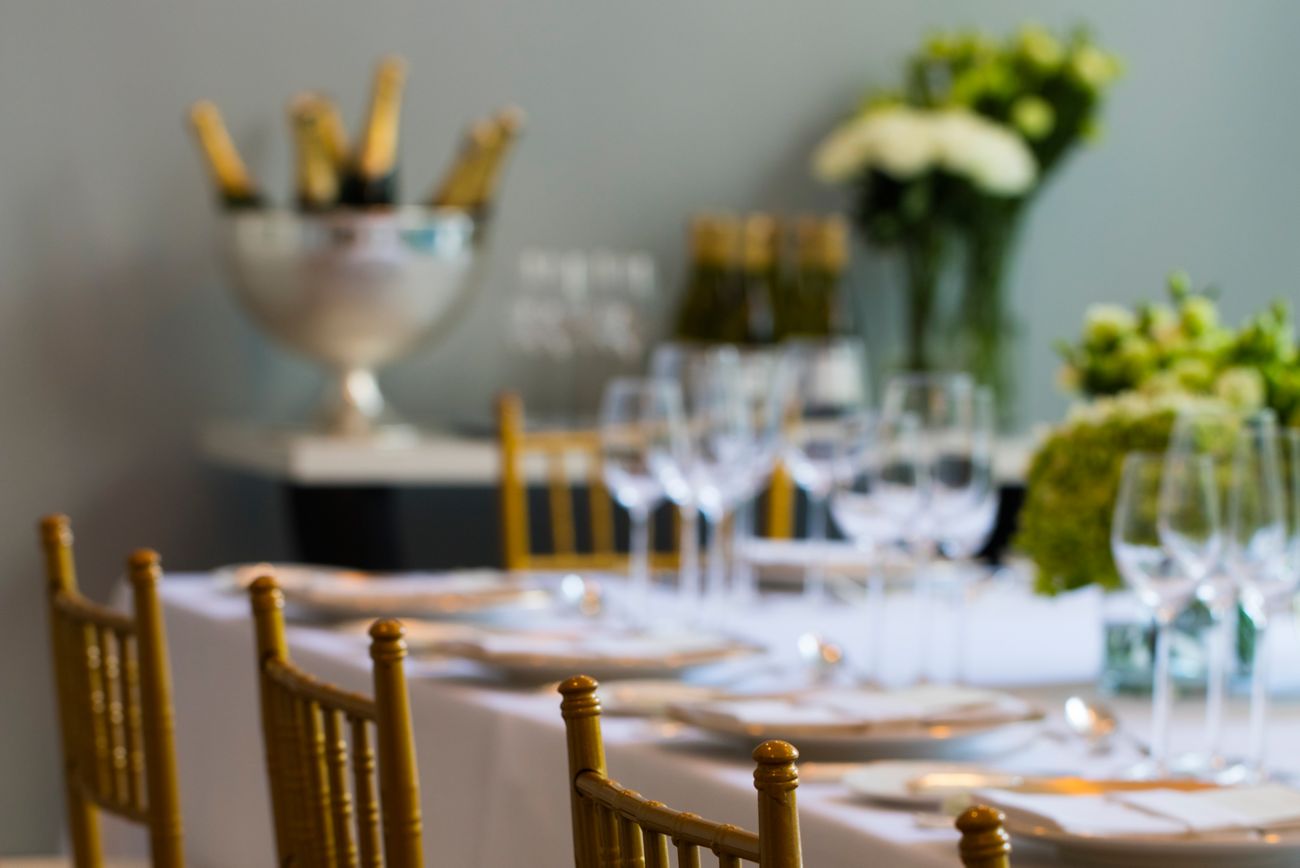 Close-up of cane chairs set at a table with a white tablecloth, green floral centerpieces and bottles of champagne