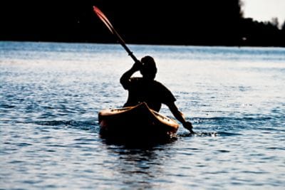 Silhouette of a man kayaking alone on the blue water of the ocean